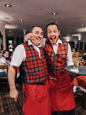 A waiter pouring wine infront of a delighted customer